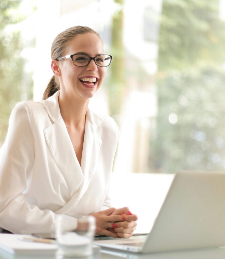 Cheerful businesswoman in glasses working on a laptop, in a bright and modern office setting.